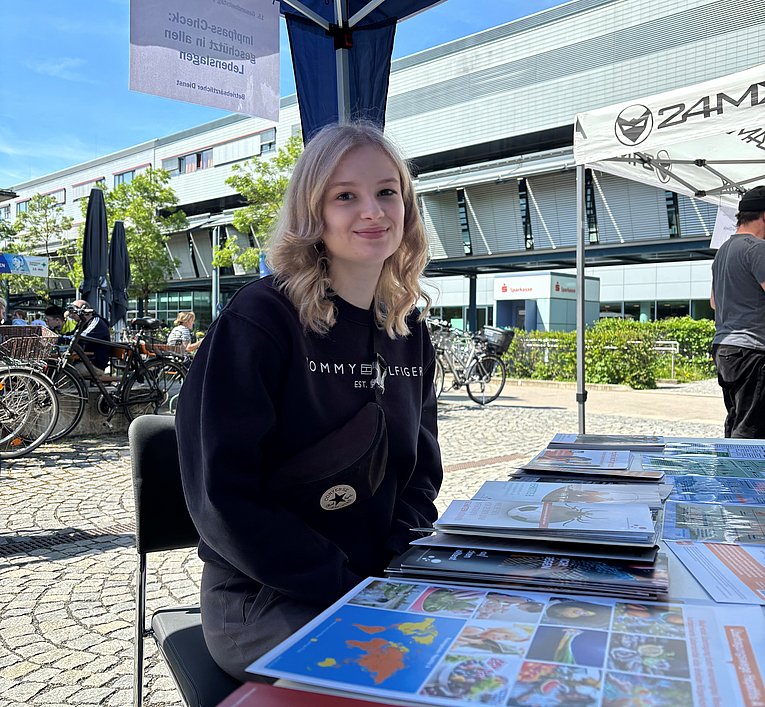 Emely Hofbauer_Gesundheitstag UKER_2025 Junge Frau sitzt an einem Infostand im Freien und lässt sich zu Ihrem Impfpass beraten