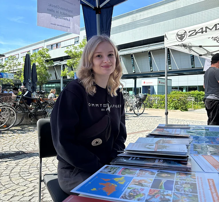 Junge Frau sitzt an einem Infostand im Freien und lässt sich zu Ihrem Impfpass beraten